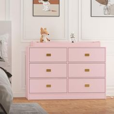 a pink dresser in a white bedroom with pictures on the wall above it and a teddy bear sitting on top