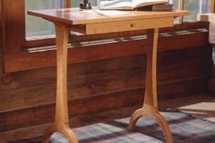 a wooden desk with an open book on it in front of a window sill