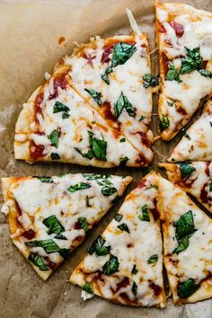 four slices of pizza with cheese and spinach on top sitting on a piece of parchment paper