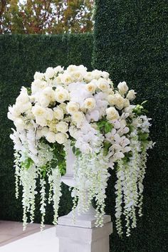 white flowers and greenery are arranged in an urn