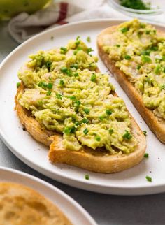 two pieces of bread with avocado on them sitting on a plate next to other plates