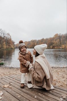 a woman and her child are sitting on the dock by the water in autumn time