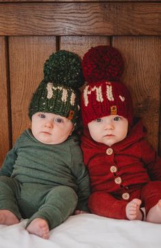 two babies laying on top of a bed wearing knitted hats with the letters h and m