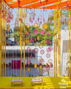 an outdoor wedding setup with yellow and pink decorations on the wall, hanging from strings