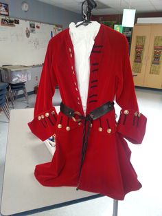 a red jacket with gold buttons on it and a white shirt underneath the coat is sitting on a table