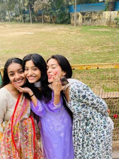 three girls are posing for the camera in front of a fence