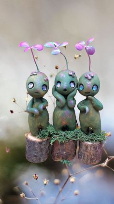 three little figurines are sitting on top of some logs with flowers growing out of them