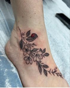 a ladybug tattoo on the foot of a woman's leg with leaves and flowers