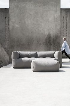 a man walking past a couch in front of a concrete wall