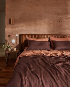 a bed with brown sheets and pillows in a room next to a wooden headboard