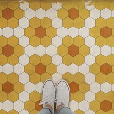 a person's feet standing on a tiled floor with orange and white hexagonal tiles