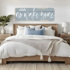 a bed with white linens and blue pillows in a large bedroom, next to a wooden sign that says no wake zone