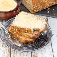 two slices of bread on a plate with butter and spoons next to the loaf