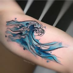 a woman's arm with a blue watercolor wave tattoo on her left shoulder