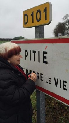 a woman writing on a street sign in front of a field with grass and trees