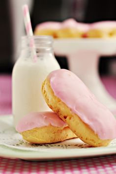 two pink frosted donuts sitting on top of a plate next to a bottle of milk