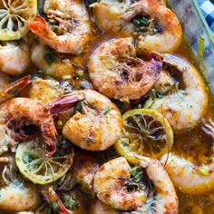 cooked shrimp with lemons and herbs in a glass dish on a checkered table cloth