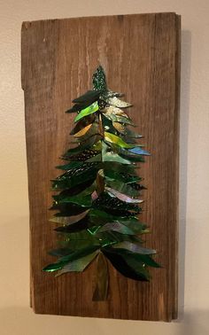 a christmas tree made out of tinsel on a wooden board with green and gold leaves