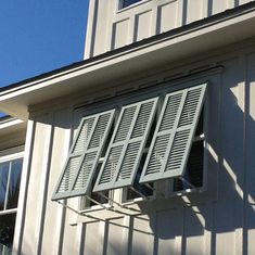 an open window on the side of a white building with shutters and a clock tower in the background