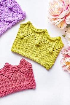 three knitted sweaters sitting next to flowers