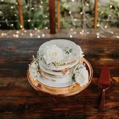 a three tiered cake with white flowers and greenery sits on a wooden table