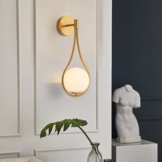 a white vase with a green plant in it next to a wall mounted light fixture