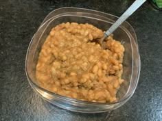 a plastic container filled with baked beans on top of a black counter next to a spoon