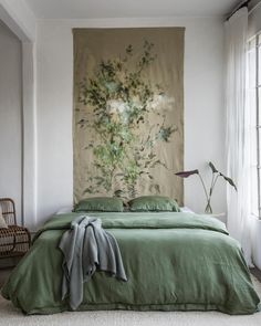 a bedroom with a large tapestry hanging on the wall next to a bed covered in green linens