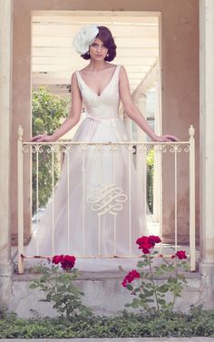 a woman in a wedding dress standing on a balcony with roses and greenery around her