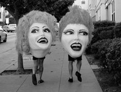 two women walking down a sidewalk with fake masks on their heads and mouths in front of them