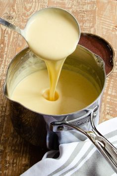 a pot filled with liquid sitting on top of a wooden table next to a spoon