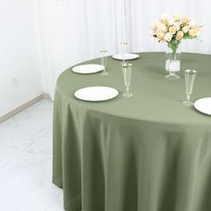 a green table cloth with white plates and flowers in vases on the top one