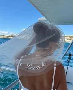 the back of a woman wearing a veil on a boat in the ocean with water behind her