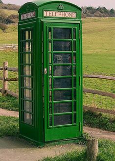 a green phone booth sitting on the side of a road next to a wooden fence