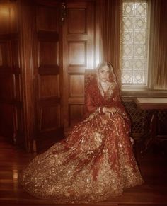 a woman in a red and gold dress sitting on a chair next to a window