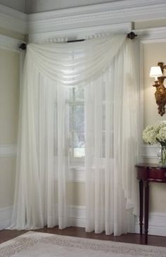 a white curtain hanging in front of a window next to a table with flowers on it