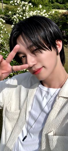 a young man making the v sign with his fingers while sitting in front of flowers