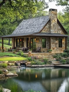 a stone house with a pond in the foreground and grass around it, surrounded by trees