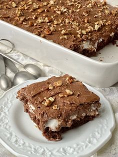 a piece of chocolate dessert on a plate next to a baking dish with spoons