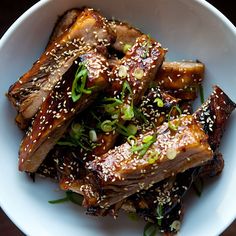 a white bowl filled with meat covered in sesame seeds and garnished with green onions