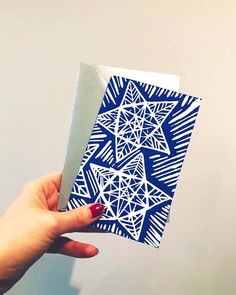 a hand holding up a blue and white paper with an intricate design on the front