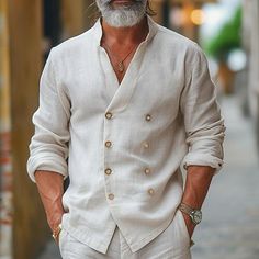 a man with a beard and white shirt is walking down the street wearing sunglasses on his head