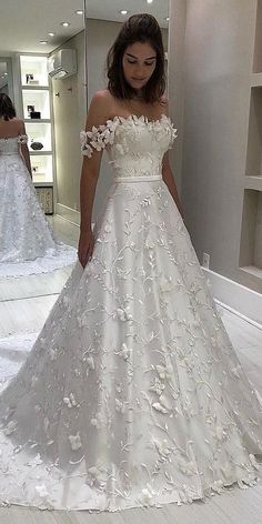 a woman standing in front of a mirror wearing a wedding dress with flowers on it