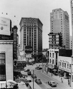 an old black and white photo of cars driving down the street in front of tall buildings