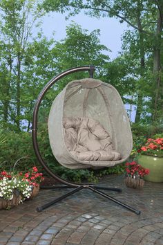 a swing chair sitting on top of a brick patio next to potted plants and flowers