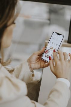 a woman is looking at her phone while sitting in front of a computer screen and holding it up