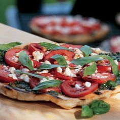 a pizza topped with tomatoes and spinach on top of a wooden cutting board next to other food items