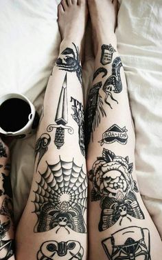 a person with tattoos on their legs laying in bed next to a cup of coffee