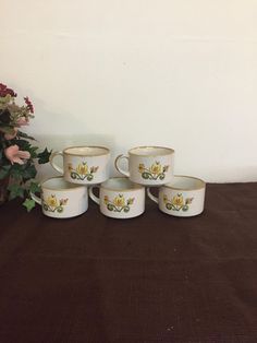 four coffee mugs sitting on top of a table next to a vase with flowers