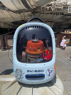 an orange and blue robot sitting on top of a wooden table next to a building